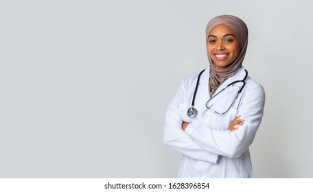 Medical Care For Muslim Women. Portrait Of Smiling Black Female Doctor In Hijab And White Coat Posing With Folded Arms Over Light Background, Panorama