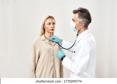 Medical Care. Professional Male Doctor In Medical Uniform And Protective Mask Using Stethoscope, Checking Lungs And Heart Of A Young Woman, Female Patient. Healthcare, Medicine. Medical Consultation