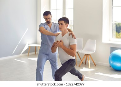 Medical Center Specialist Helping Young Man Recover After Trauma. Professional Physiotherapist Helping Male Athlete Do Forward Lunges Exercise During Physiotherapy Rehabilitation After Sports Injury