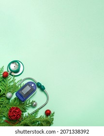 Medical Concept: Celebrating Christmas In Healthcare. Top View Of A Flat Lay Close-up Of A Stethoscope, Pulse Oximeter With Fir Branches On A Green Background. With Copy Space.Vertical Photo