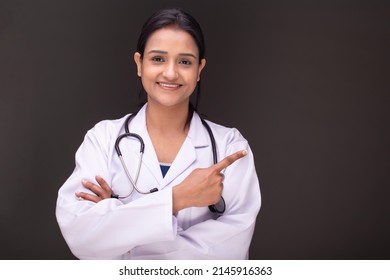 Medical Concept Of Indian Beautiful Female Doctor In White Coat With Stethoscope, Waist Up. Medical Student. Woman Hospital Worker Looking At Camera And Smiling, Studio, Gray Background