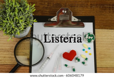 Medical concept : Listeria text ,magnifier,pills and syringe on wooden background