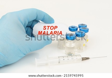 Medical concept. In the man's hand is a piece of paper with the inscription - STOP MALARIA, next to it lies a syringe and injection jars.