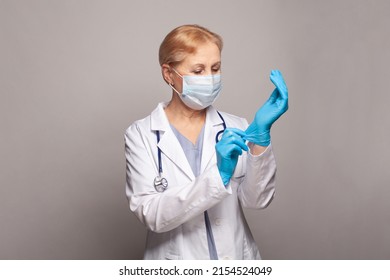 Medical Concept Of Mature Female Doctor In White Coat With Stethoscope Putting On Medical Gloves