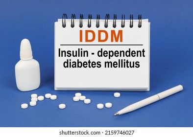 Medical concept. On a blue background, a pen, tablets and a notepad with the inscription - IDDM Insulin-dependent diabetes mellitus