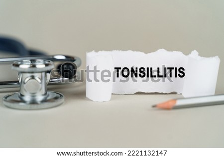 Medical concept. On a gray background, a stethoscope, a pencil and a paper plate with the inscription - Tonsillitis