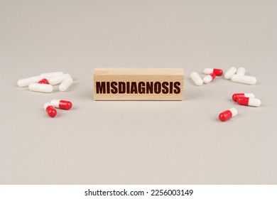 Medical concept. On a gray surface are tablets, capsules and a wooden plate with the inscription - Misdiagnosis - Shutterstock ID 2256003149