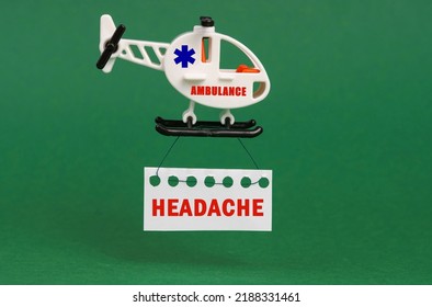 Medical concept. On a green surface, an ambulance helicopter with a sign - HEADACHE