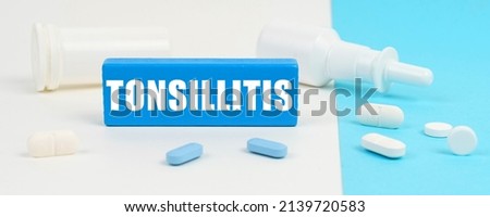 Medical concept. On a white and blue surface are pills, a spray and a wooden sign with the inscription - Tonsillitis