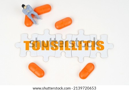 Medical concept. On the white surface of the tablet, a miniature human figure and puzzles with the inscription - Tonsillitis