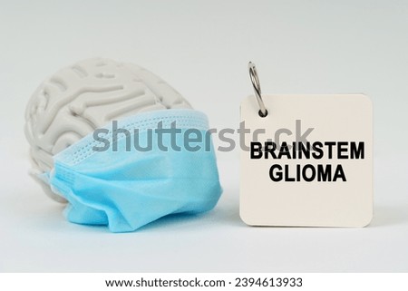 Medical concept. On a white surface there is a brain with a blue mask and a notepad with the inscription - Brainstem glioma