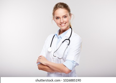 Medical Concept Of Young Beautiful Female Doctor In White Coat With Phonendoscope, Waist Up. Woman Hospital Worker Looking At Camera And Smiling, Studio, Grey Background