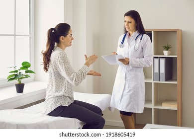Medical consultation and health screening. Woman talking to female doctor sitting on examination bed at clinic. General practitioner, therapeutist or gynecologist listening to patient and taking notes