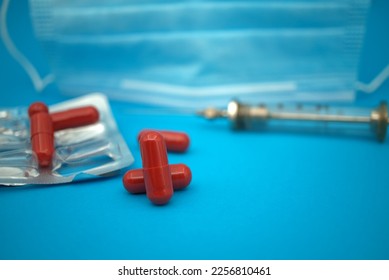 Medical, Covid-19 and healthcare background with red capsules scattered on blue alongside an empty blister pack with syringe and face mask - Shutterstock ID 2256810461