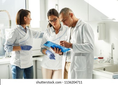 Medical Dentist Team In Dental Office Discuss About Practice And Examining List Of Patients.