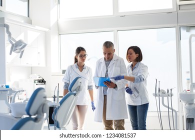 Medical Dentist Team In Dental Office Examining List Of Patients.