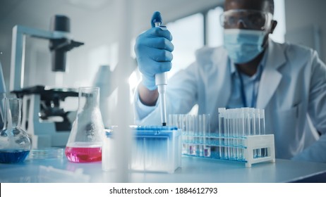 Medical Development Laboratory: Black Scientist Wearing Face Mask Uses Micro Pipette, Filling Test Tube With Liquid, Conducting Experiment. Pharmaceutical Lab With Medicine, Biotechnology Researchers