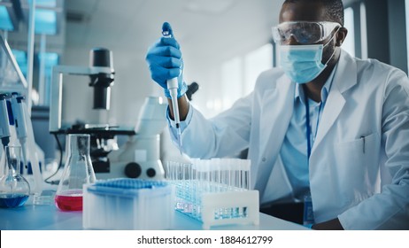 Medical Development Laboratory: Black Scientist Wearing Face Mask Uses Pipette For Filling Test Tube With Liquid, Conducting Experiment. Pharmaceutical Lab With Medicine, Biotechnology Researchers