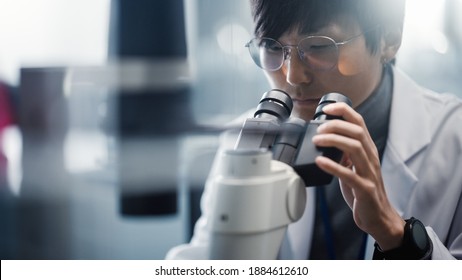 Medical Development Laboratory: Portrait of East Asian Scientist Looking Under Microscope, Analyzes Petri Dish Sample. Pharmaceutical Lab doing Medicine, Biotechnology, Microbiology, Drugs Research. - Powered by Shutterstock