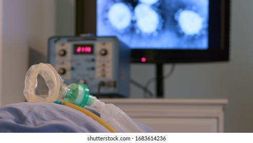 A medical device used to assist in breathing lays idle on a hospital bed with an image of the coronavirus COVID19 on a monitor in the background.