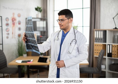 Medical Diagnosis Concept. Portrait Of Male Arab Doctor Oncologist Physician Examining Lungs X-ray Computerized Tomography Scan, Working In His Office In Modern Clinic. Side Angle View Indoor Shot.