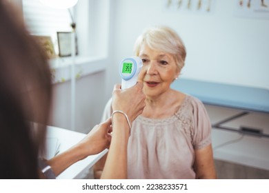 Medical doctor checking senior patient temperature with infrared thermometer. Receptionist checking fever middle age woman by digital thermometer for fever scan. Healthcare concept - Powered by Shutterstock