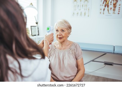 Medical doctor checking senior patient temperature with infrared thermometer. Receptionist checking fever middle age woman by digital thermometer for fever scan. Healthcare concept - Powered by Shutterstock