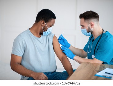 Medical doctor or nurse giving coronavirus vaccine shot to African American male patient at clinic. Young black man in face mask getting covid-19 vaccine, participating in immunization campaign