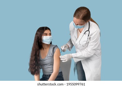 Medical Doctor Or Nurse Giving Coronavirus Vaccine Shot To Indian Teen Girl Over Blue Studio Background. Female Teenager In Face Mask Getting Covid-19 Vaccine, Participating In Immunization Campaign