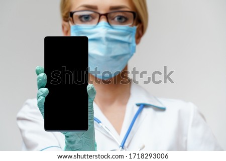 medical doctor nurse woman wearing protective mask and gloves - using mobile phone