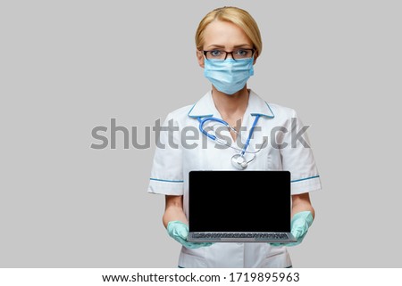 medical doctor nurse woman wearing protective mask and gloves - holding laptop