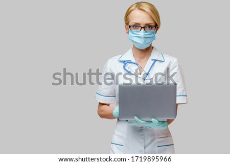 medical doctor nurse woman wearing protective mask and gloves - holding laptop