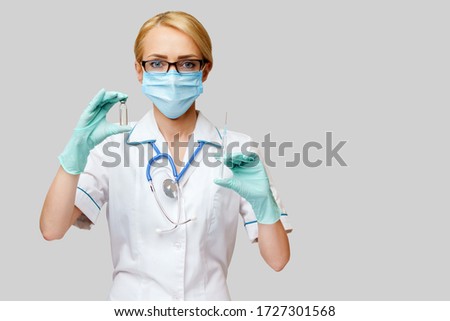 medical doctor nurse woman wearing protective mask and gloves - holding bottle of vaccine medicine and syringe