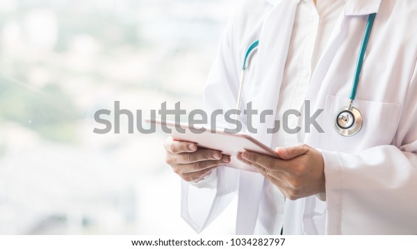 Medical doctor or physician consulting patient\'s health\
online using internet mobile digital tablet in clinic or hospital\
office for professional emergency healthcare assistance service\
concept 