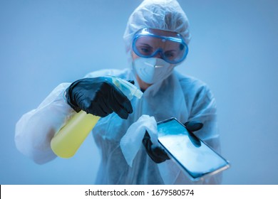 Medical Doctor, Scientist In Full Body Suit For Prevention From Viruses And Diseases Holding A Antiseptic Tissue For Smartphone Disinfection.