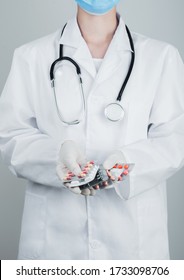 Medical Doctor Wearing Clear Latex Gloves Holding Stack Of Different Pills On Grey Hospital Wall. Antibiotics And Virus Treatment Tablets.