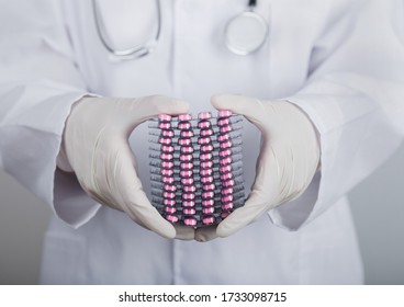 Medical Doctor Wearing Clear Latex Gloves Holding Stack Of Different Pills On Grey Hospital Wall.