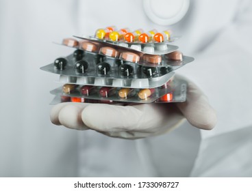 Medical Doctor Wearing Clear Latex Gloves Holding Stack Of Different Pills On Grey Hospital Wall. Antibiotics And Virus Treatment Tablets.