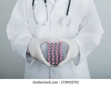 Medical Doctor Wearing Clear Latex Gloves Holding Stack Of Different Pills, Antibiotics And Virus Treatment Tablets On Grey Hospital Wall.