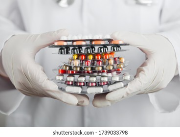 Medical Doctor Wearing Clear Latex Gloves Holding Stack Of Different Pills, Antibiotics And Virus Treatment Tablets On Grey Hospital Wall.