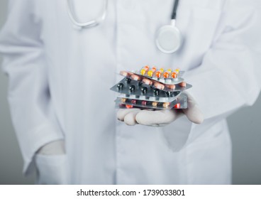 Medical Doctor Wearing Clear Latex Gloves Holding Stack Of Different Pills On Grey Hospital Wall. Antibiotics And Virus Treatment Tablets.