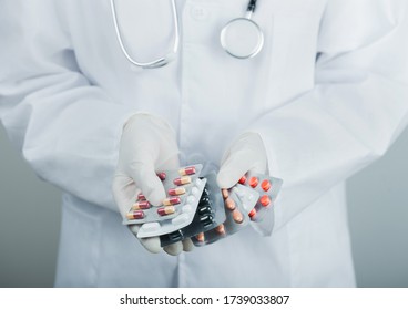 Medical Doctor Wearing Clear Latex Gloves Holding Stack Of Different Pills On Grey Hospital Wall. Antibiotics And Virus Treatment Tablets.