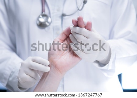 Medical doctor wearing latex gloves examining patient’s pulse in hospital setting