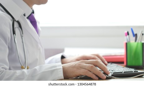 Medical Doctor Working On Laptop In His Cabinet And Clicking Computer Mouse.