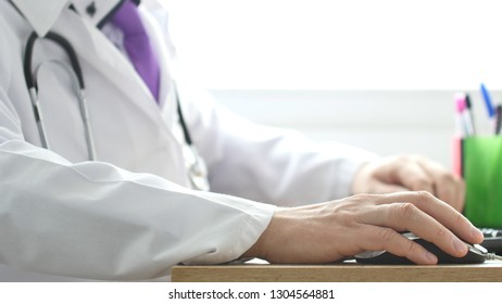 Medical Doctor Working On Laptop In His Cabinet And Clicking Computer Mouse.