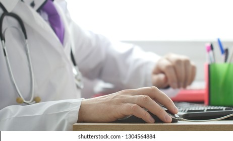 Medical Doctor Working On Laptop In His Cabinet And Clicking Computer Mouse.