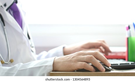 Medical Doctor Working On Laptop In His Cabinet And Clicking Computer Mouse.