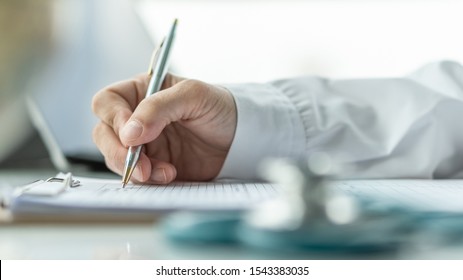 Medical Doctor Writing On Patient Personal Health Care Record Discharge Form, Or Prescription Paperwork In Hospital Office, Clinic Center For Healthcare And Life Insurance Concept