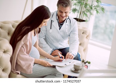 Medical Documents. Delighted Positive Nice Woman Sitting In The Hospital Room And Talking To Her Doctor While Signing A Medical Agreement