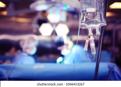 Medical dropper hanging on a tripod against the background of a team of surgeons conducting an operation.